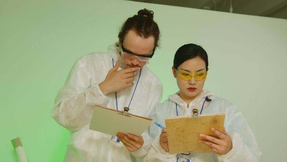 Two researchers in laboratory attire reviewing experiment data on clipboards.