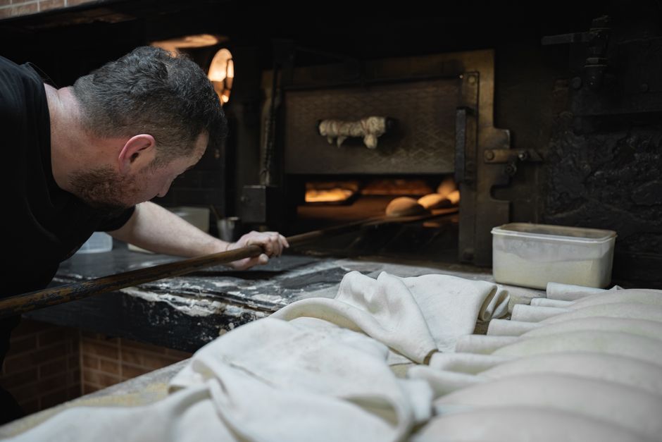 A baker using a peel to place dough into a traditional stone oven.