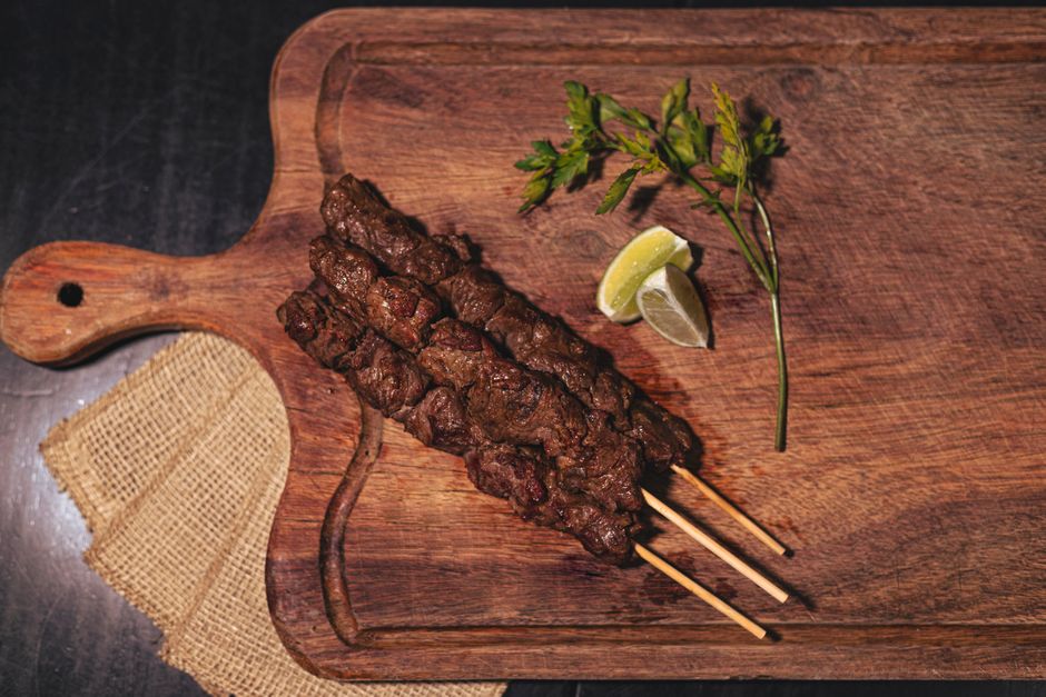 Succulent grilled meat skewers on a wooden board with lemon wedges and fresh greens.